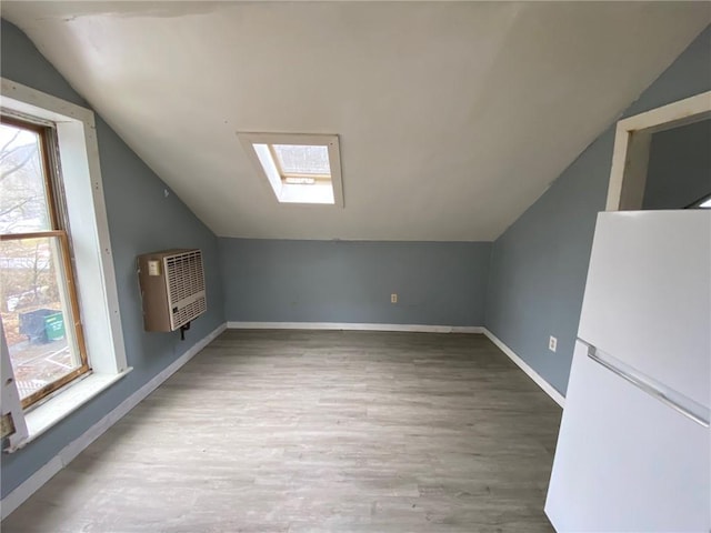 additional living space with vaulted ceiling with skylight, baseboards, heating unit, and wood finished floors