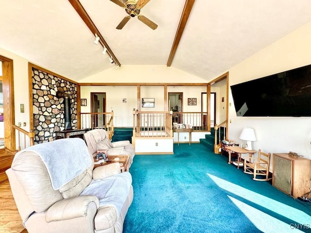 living room with carpet flooring, a wood stove, lofted ceiling with beams, rail lighting, and ceiling fan