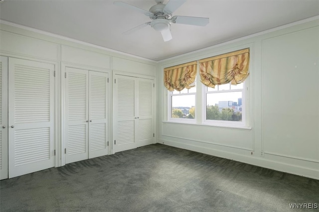 unfurnished bedroom with ceiling fan, ornamental molding, two closets, and dark carpet