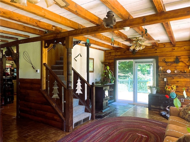 interior space featuring a wood stove, ceiling fan, dark parquet floors, beamed ceiling, and wood ceiling