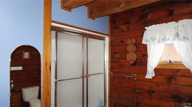 bathroom featuring toilet, beam ceiling, and wooden walls