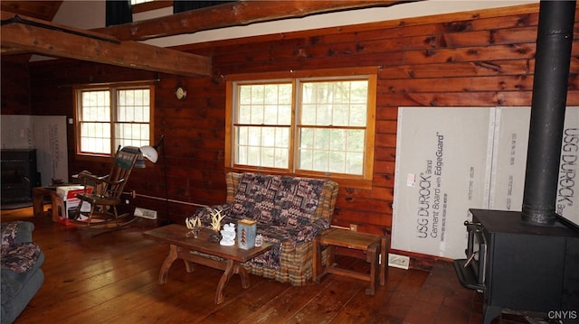 living room with wood-type flooring, a wood stove, beam ceiling, and a healthy amount of sunlight