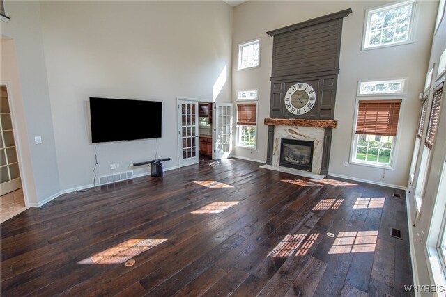 unfurnished living room with a towering ceiling, dark hardwood / wood-style floors, and a high end fireplace