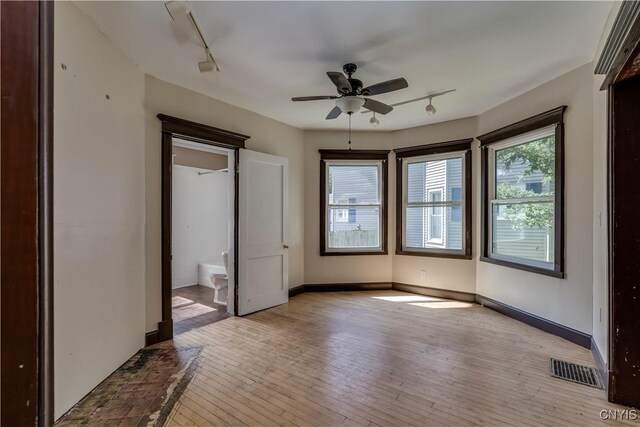 unfurnished bedroom with rail lighting, ceiling fan, ensuite bathroom, and light hardwood / wood-style floors