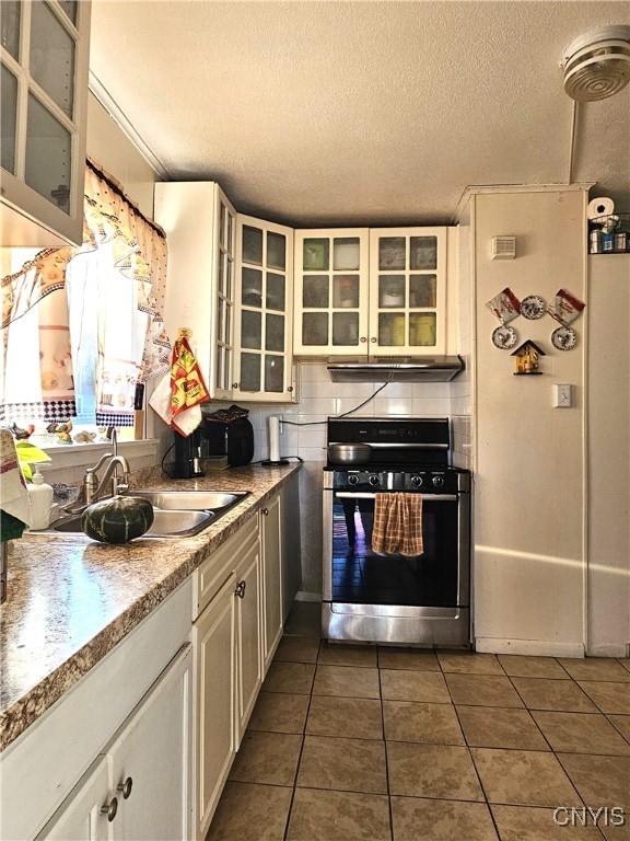 kitchen featuring a textured ceiling, dark tile patterned floors, range, sink, and white cabinets