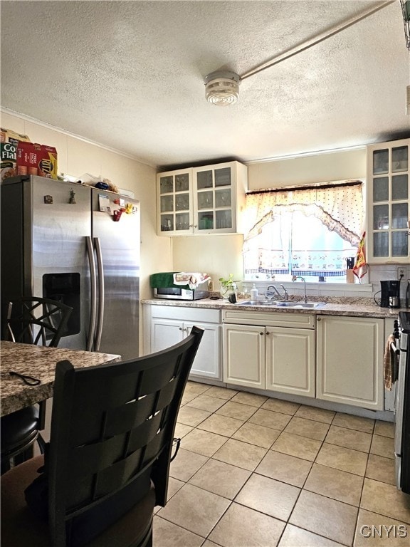 kitchen with a textured ceiling, light tile patterned floors, sink, stainless steel refrigerator with ice dispenser, and white cabinets