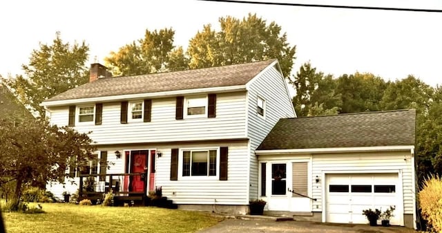 colonial house with a front yard, roof with shingles, an attached garage, a chimney, and aphalt driveway