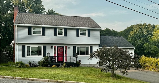 colonial inspired home with aphalt driveway, a chimney, a front yard, and roof with shingles