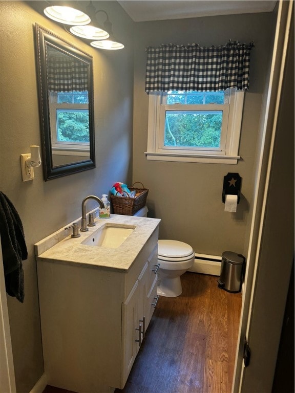 bathroom with wood-type flooring, vanity, toilet, and a baseboard heating unit