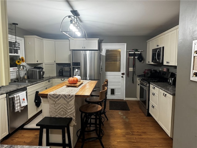 kitchen with dark wood-type flooring, pendant lighting, stainless steel appliances, wooden counters, and sink