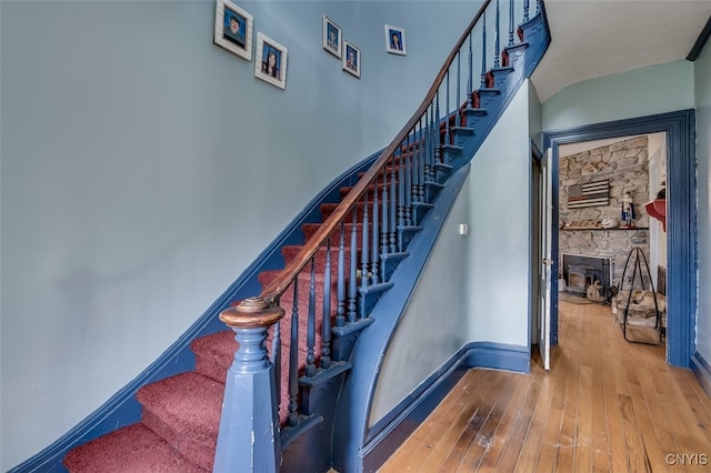 staircase with a stone fireplace and hardwood / wood-style flooring