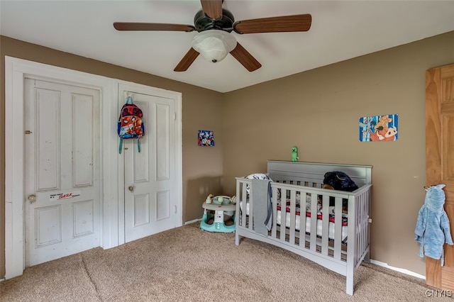 carpeted bedroom featuring ceiling fan and a crib