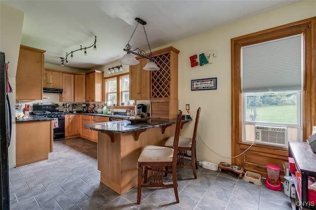 kitchen featuring pendant lighting, black stove, kitchen peninsula, sink, and dark stone counters