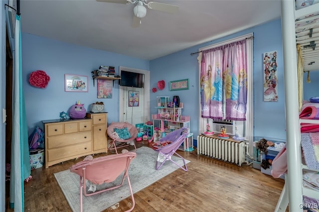 recreation room with cooling unit, ceiling fan, radiator heating unit, and dark hardwood / wood-style flooring