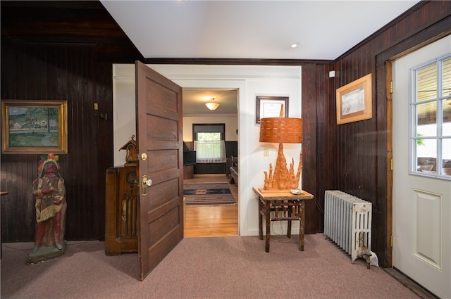 hallway with ornamental molding, carpet floors, radiator, and wood walls