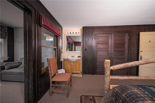 bedroom with connected bathroom, wood walls, sink, and carpet flooring