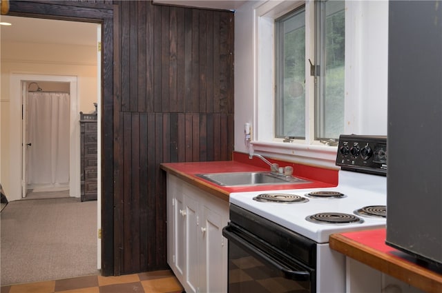 kitchen with light colored carpet, electric range, sink, wooden walls, and white cabinets