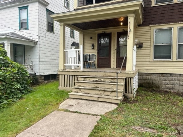 view of exterior entry with a lawn and covered porch