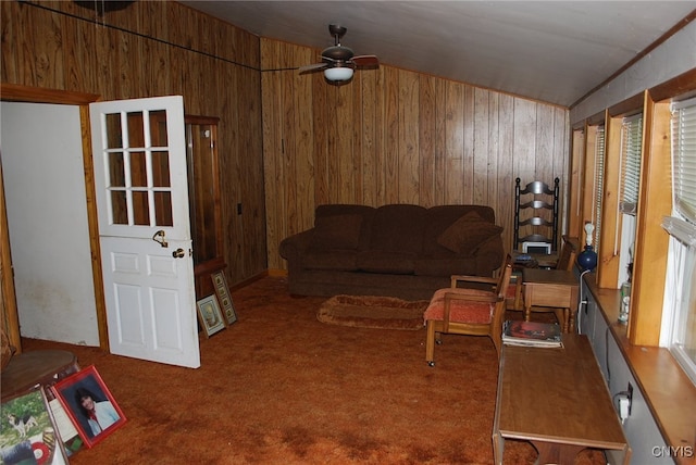 living room featuring lofted ceiling, ceiling fan, wooden walls, and carpet