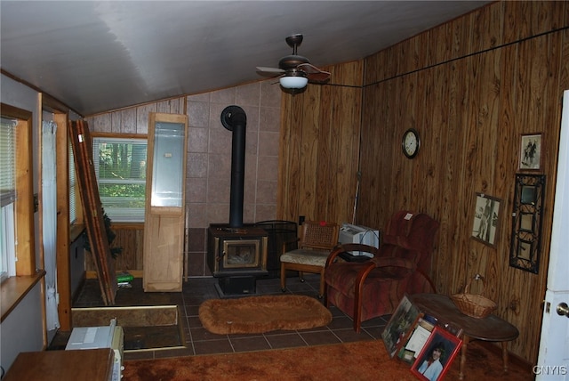 tiled living room with a wood stove, ceiling fan, wooden walls, and vaulted ceiling