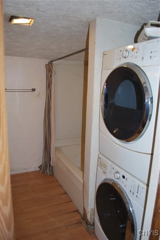 laundry room featuring a textured ceiling, stacked washer and clothes dryer, and hardwood / wood-style floors