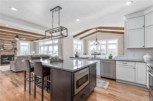 kitchen with white cabinets, appliances with stainless steel finishes, a wealth of natural light, and a stone fireplace