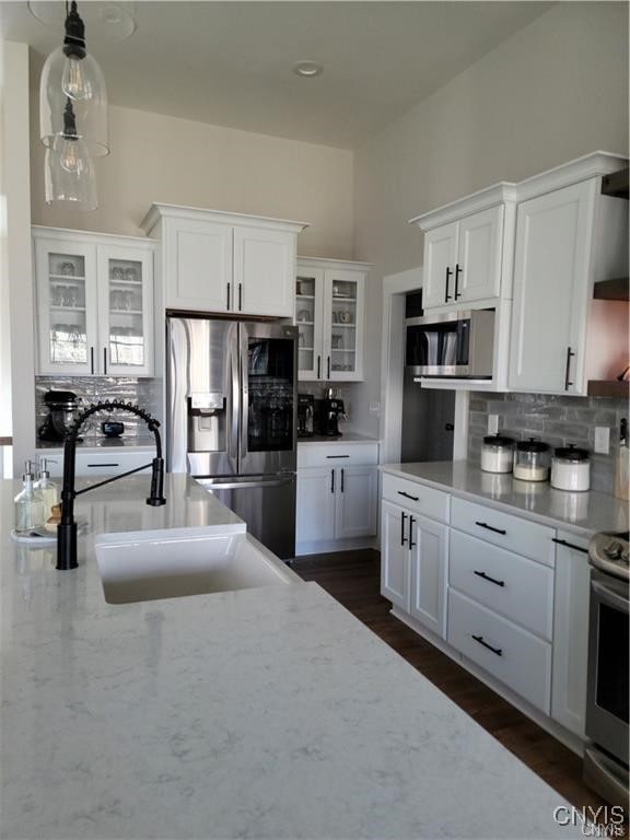 kitchen featuring backsplash, dark wood-type flooring, hanging light fixtures, appliances with stainless steel finishes, and white cabinets