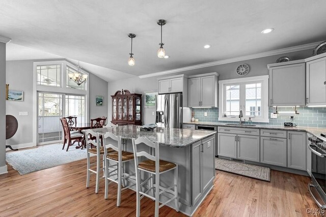 kitchen with vaulted ceiling, light wood-type flooring, appliances with stainless steel finishes, plenty of natural light, and a kitchen island