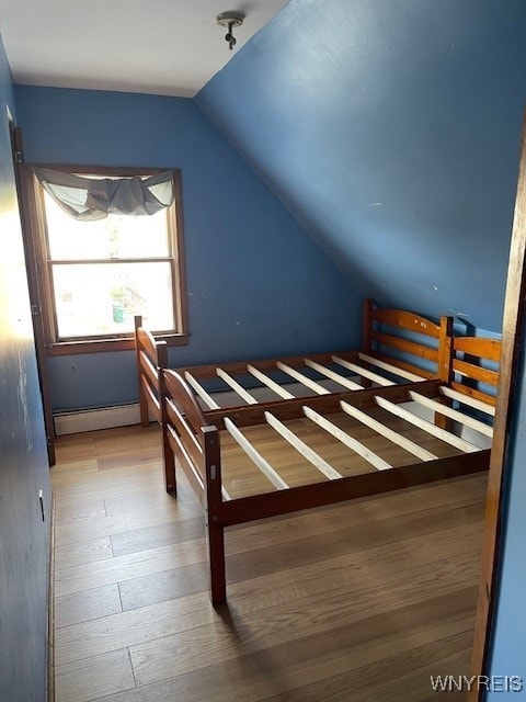 unfurnished bedroom featuring wood-type flooring, vaulted ceiling, and baseboard heating