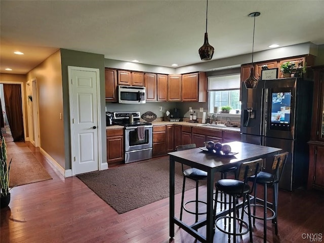 kitchen with stainless steel appliances, dark hardwood / wood-style flooring, sink, pendant lighting, and a breakfast bar