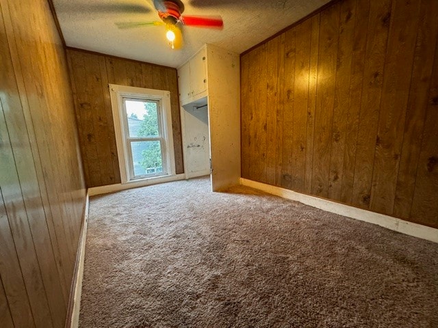 unfurnished room featuring carpet, wood walls, and a textured ceiling