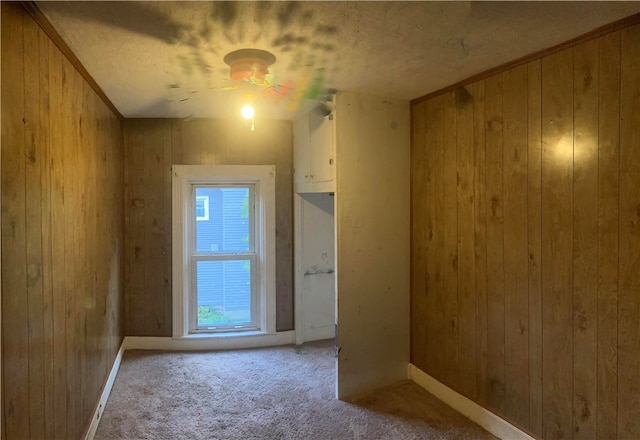 unfurnished room featuring light carpet, wood walls, and a textured ceiling