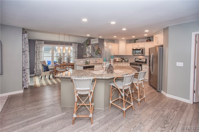 kitchen featuring a breakfast bar area, stainless steel appliances, pendant lighting, light stone counters, and light hardwood / wood-style flooring