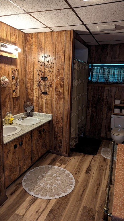 bathroom with vanity, wood-type flooring, toilet, wooden walls, and a drop ceiling