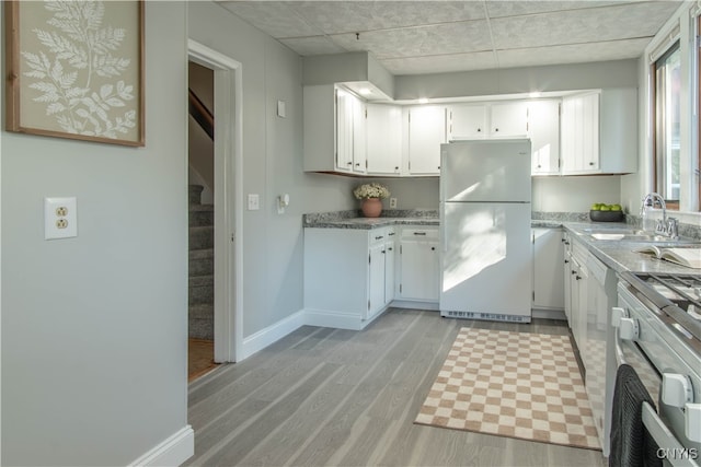 kitchen with white cabinets, stove, light wood-type flooring, sink, and white refrigerator