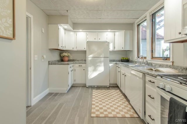 kitchen with white appliances, light stone countertops, sink, light hardwood / wood-style floors, and white cabinets