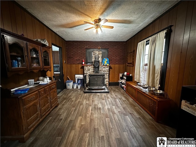 office area featuring ceiling fan, dark hardwood / wood-style floors, wood walls, and a wood stove