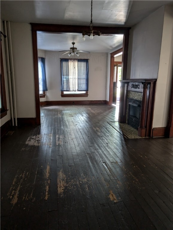 unfurnished living room featuring ceiling fan, a fireplace, dark wood-type flooring, and a wealth of natural light