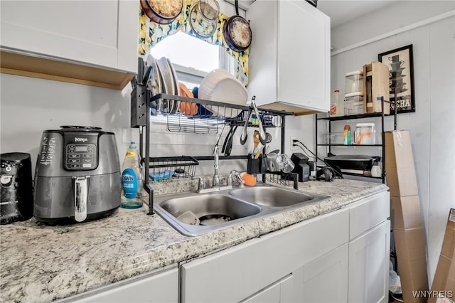 kitchen featuring light stone counters, sink, and white cabinetry