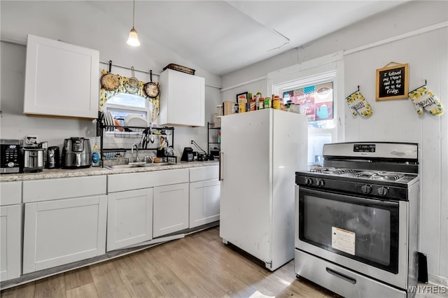 kitchen with white refrigerator, light wood-type flooring, gas range, lofted ceiling, and white cabinetry