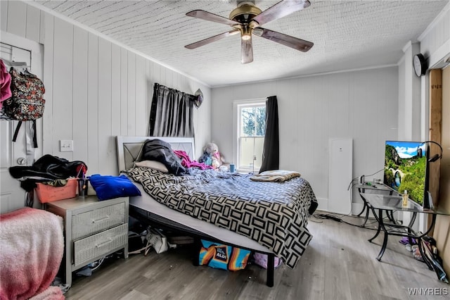 bedroom featuring light wood-type flooring, crown molding, ceiling fan, and wood walls