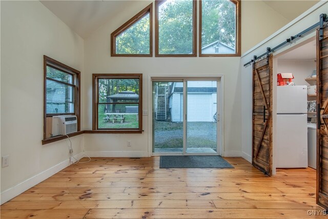 doorway featuring high vaulted ceiling, cooling unit, light hardwood / wood-style floors, and a barn door