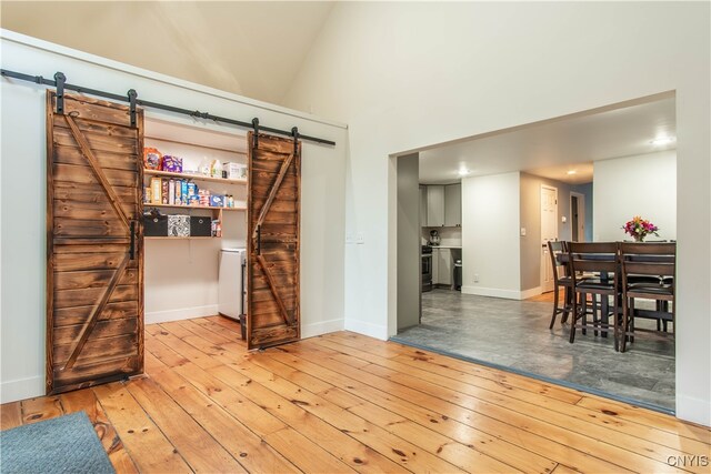 living room with light wood-type flooring, a barn door, and high vaulted ceiling