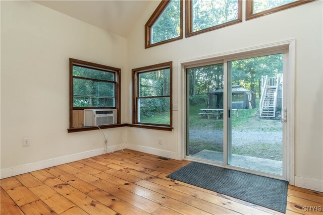 doorway to outside featuring cooling unit, light hardwood / wood-style flooring, high vaulted ceiling, and a wealth of natural light