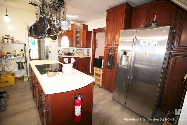 kitchen with pendant lighting, wood-type flooring, a kitchen island, black electric cooktop, and stainless steel fridge