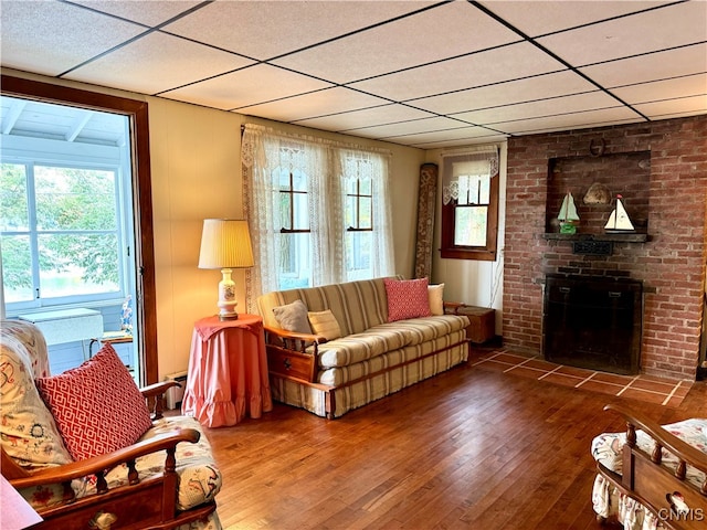 living room with a brick fireplace, hardwood / wood-style flooring, and a drop ceiling