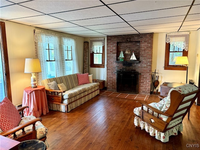 living room featuring a fireplace, a drop ceiling, and dark wood-type flooring