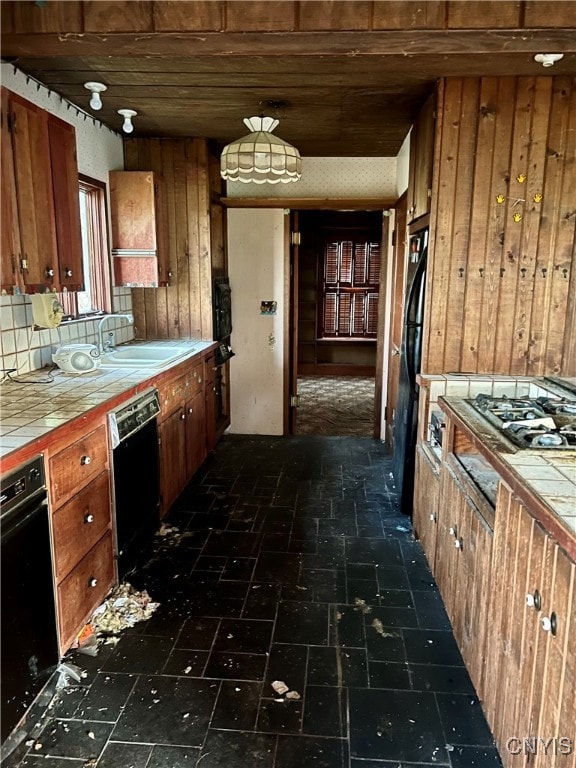 kitchen featuring wooden walls, black appliances, tile counters, and sink