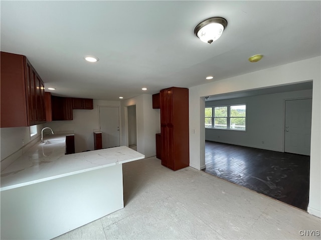 kitchen featuring light wood-type flooring, light stone counters, kitchen peninsula, and sink