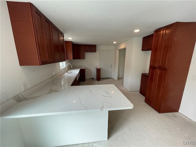 kitchen featuring a breakfast bar, light stone counters, kitchen peninsula, and sink